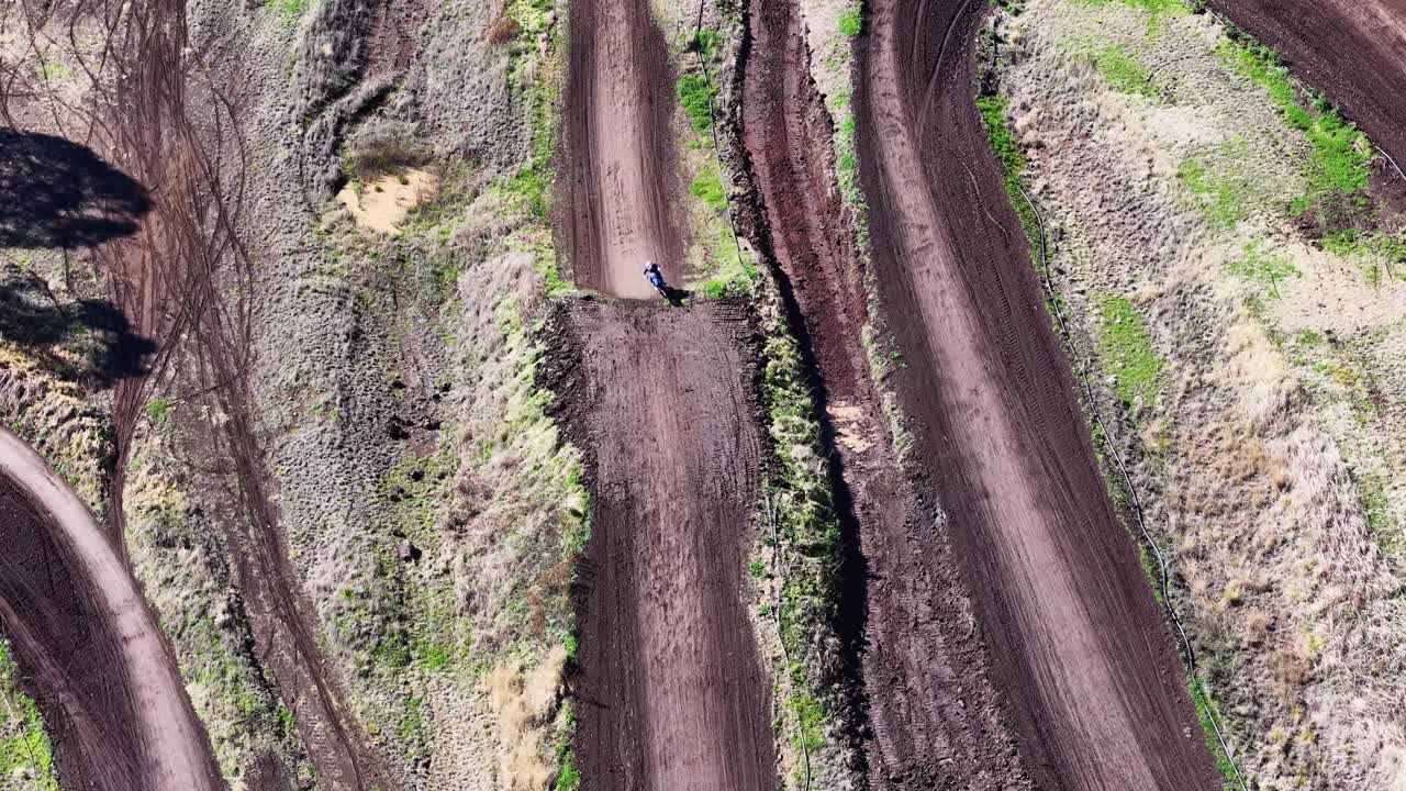 Motorbike rider navigates dirt track curve in bright daylight, captured from high aerial perspective
