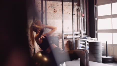 Lockdown-Shot-Of-Young-Female-Athlete-Doing-Sit-Ups-On-Exercise-Ball-In-Gym