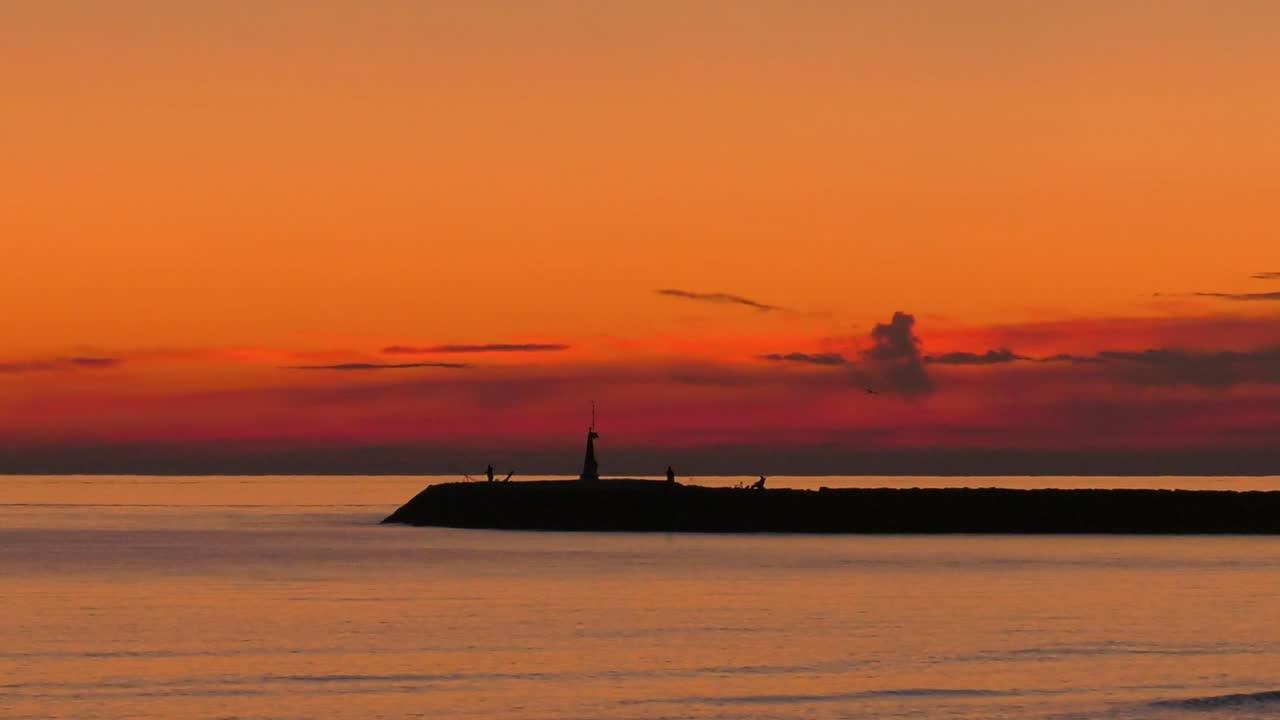 silueta del malecón del puerto contra el cielo anaranjado del amanecer y el mar en calma, mediterráneo