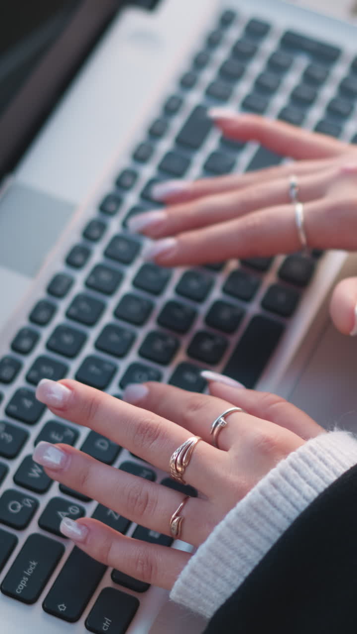 primer plano de manos escribiendo en el teclado de la computadora portátil con uñas pulidas y anillos elegantes, reflejándose en la pantalla, mostrando un ambiente tecnológico y profesional