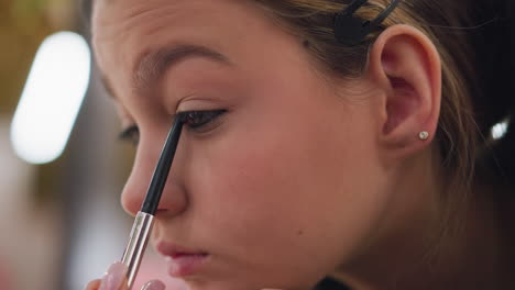 close-up of young girl applying makeup on eyelid, carefully using pencil on her eye while blinking, the detailed process of applying eye makeup and enhancing eye area captured in vibrant focus