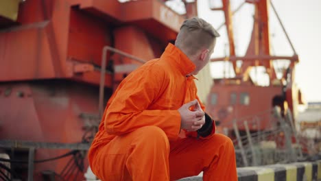 young man in orange uniform sitting during his break by the sea in the harbor