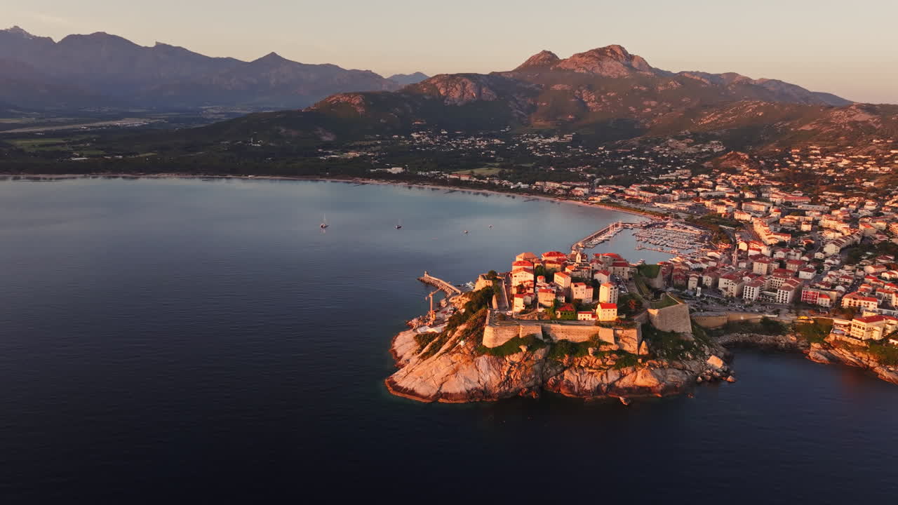 Cinematic aerial drone shot over the citadel of Calvi at sunrise. High view of the fortress at dawn in Corsica. Golden hour, warm colors
