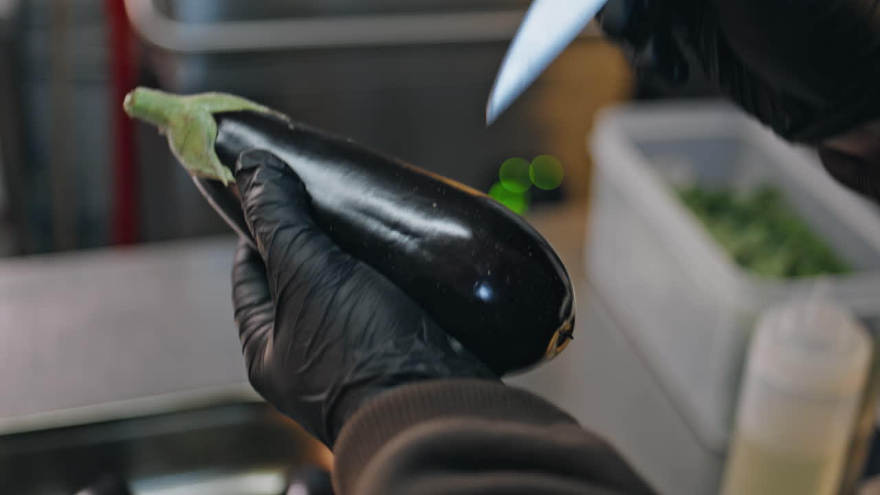 Chef hands holding aubergine making cuts knife in restaurant kitchen closeup