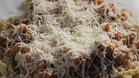 close up of sprinkling shredded cheese on pasta bolognese, static shot