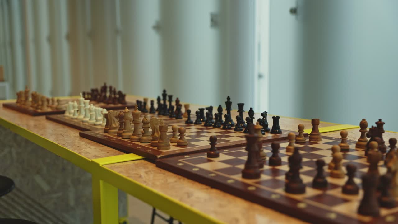 A long wooden table with chessboards in a spacious, well-lit library area, inviting visitors to play and engage.