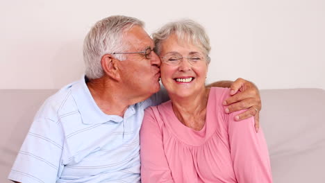 Senior-couple-sitting-on-sofa-smiling-at-camera