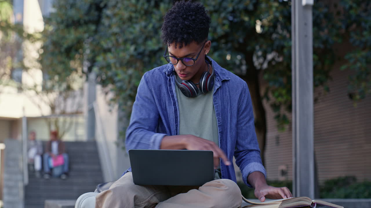 Young man studying outdoors with laptop and books