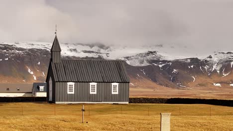 lonely small town church búðakirkja, picturesque snow covered mountains in background, iceland