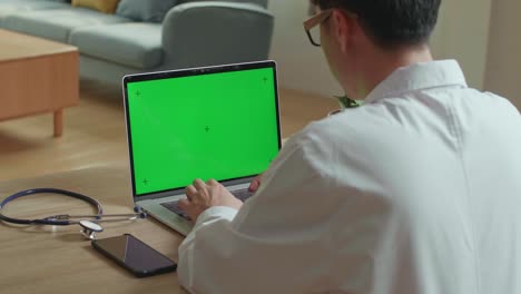 male doctor working on laptop computer with green screen display, video in 4k