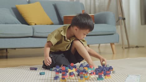 full body of asian kid assemble the construction set colorful plastic toy brick on a mat at home