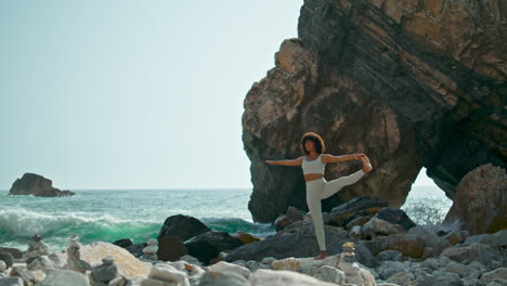 Woman-practicing-yoga-standing-one-leg-on-rocky-seashore-summer-day-vertical