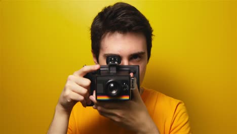 Retrato-De-Un-Atractivo-Joven-Milenario-Tomando-Fotografías-En-Una-Cámara-De-Película-Antigua-Con-Fondo-Amarillo