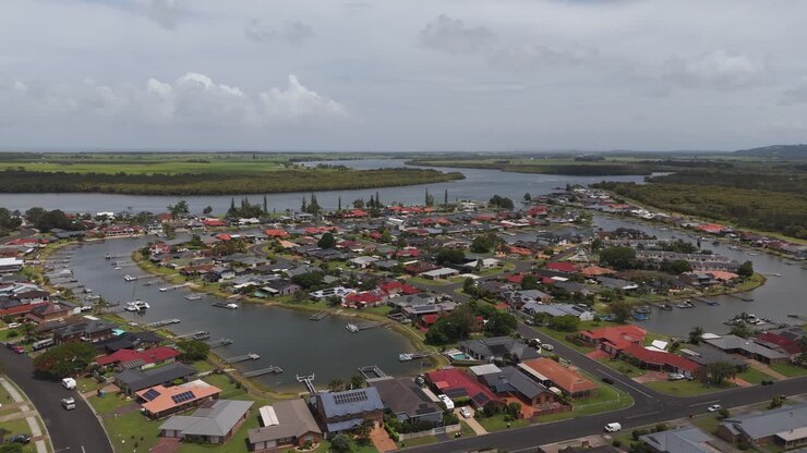 Pieni Ballinan kaupunki Australiassa pilvisenä päivänä. Yksityinen laituri ja satamalaituri pysäköityine veneineen. Ylellinen pikkukaupunki kartanoineen ja huviloineen. Laaja kiertävä ilmakuva.