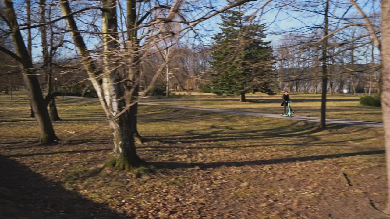 un hombre con un abrigo largo disfruta de un paseo matutino por un parque soleado en un scooter eléctrico