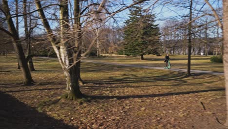 A-man-in-a-long-coat-enjoys-a-morning-ride-through-a-sunny-park-on-an-electric-scooter