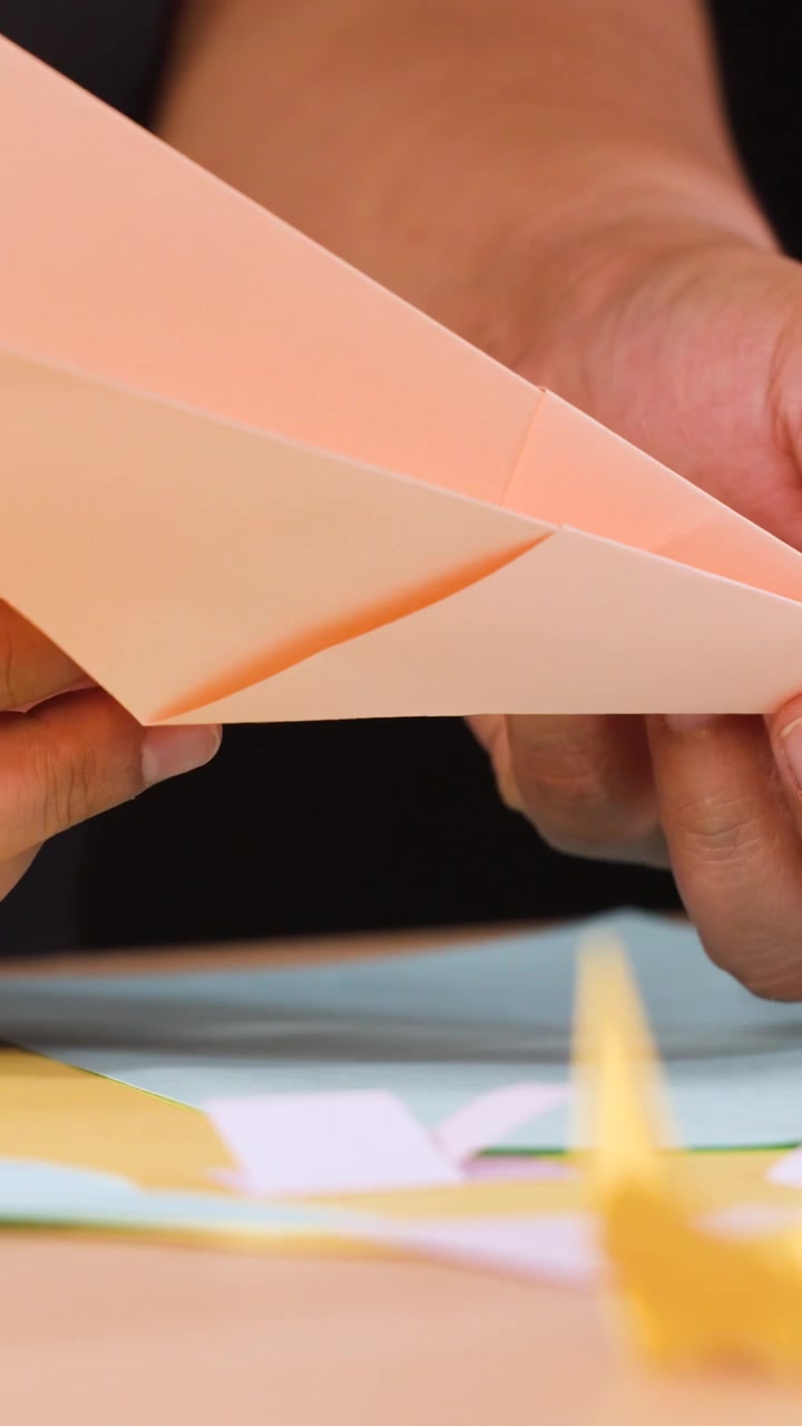 Close-up shot of hands carefully folding orange paper into an origami airplane on a table