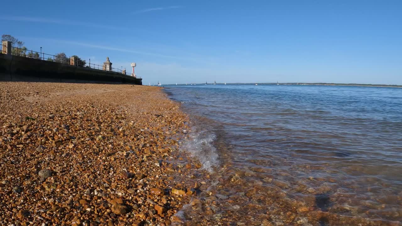 Kristallklare Wasserwellen küssen sanft den orangefarbenen Kiesstrand auf der Isle of Wight