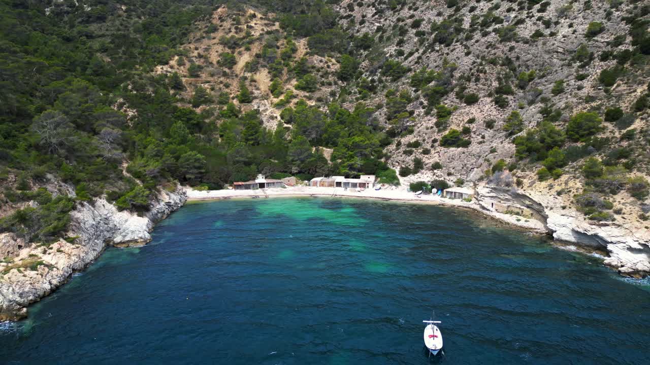 Cala Llentrisca beach with turquoise water and Barques de pescadors Huts in Ibiza, Spain, in summer. Perfect aerial view flight wide orbit overview drone