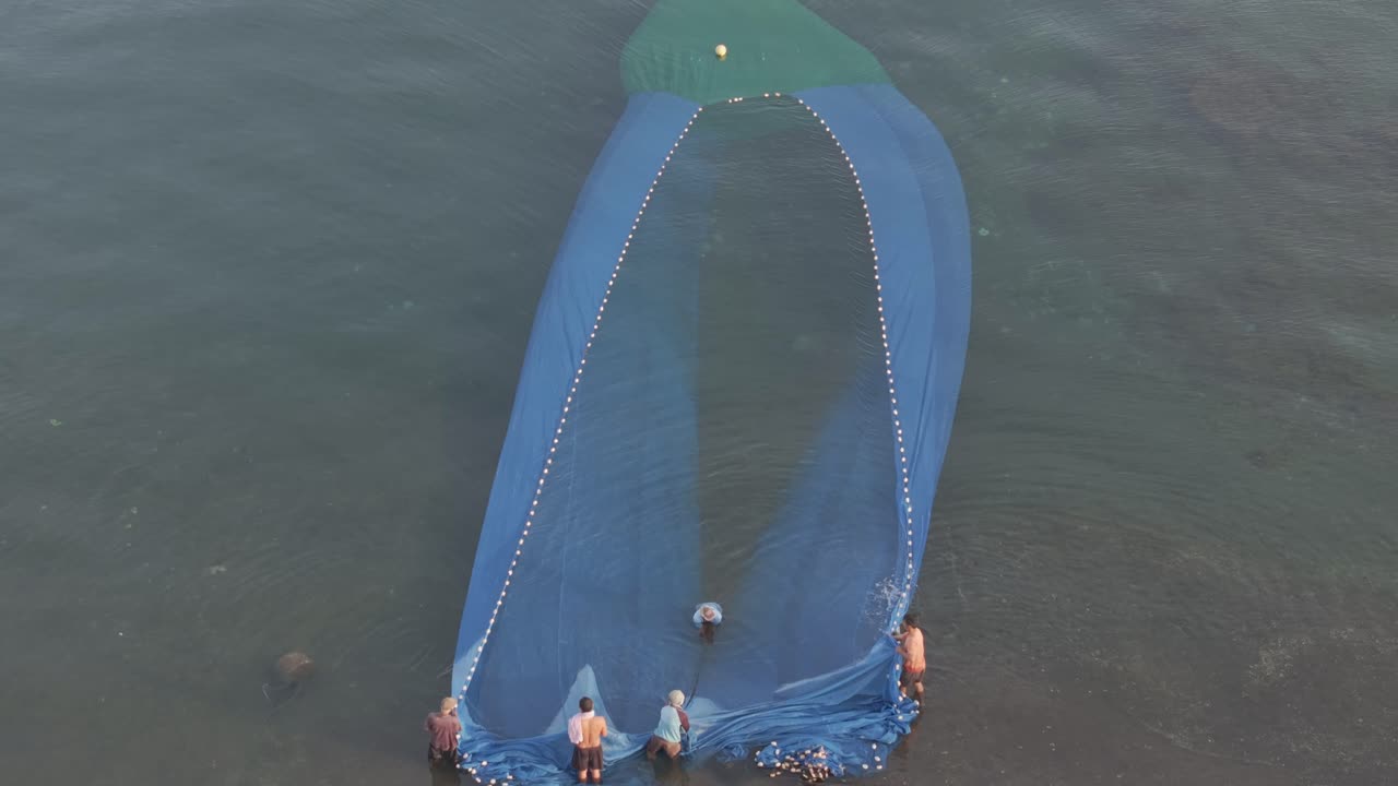 Pescatori maneggiano un'ampia rete lungo la costa tropicale in Indonesia.