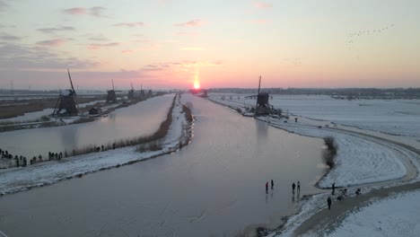 Roter-Sonnenaufgang-Am-Kinderdijk-Mit-Leuten,-Die-Sich-An-Land-Zum-Eislaufen-Bereit-Machen