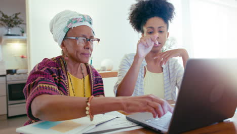 senior black woman using laptop for paying bills with help of daughter at home
