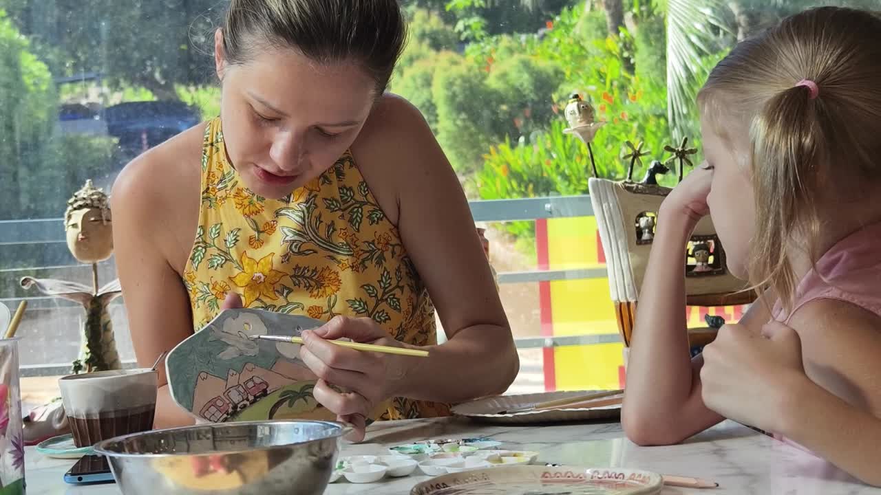 madre e hija pintando una placa de cerámica juntos