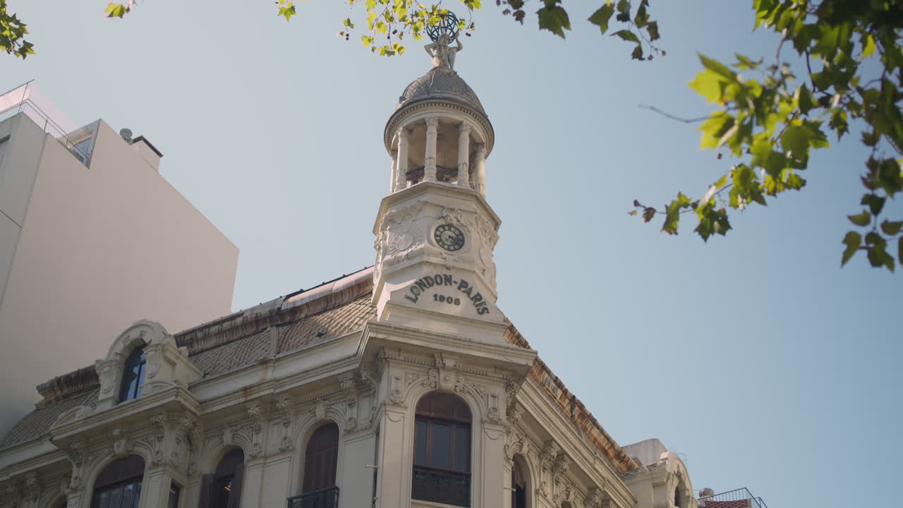 Inquadratura dal basso di una torre storica con orologio e dettagli del tetto.