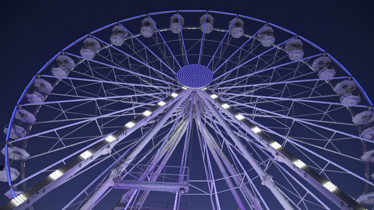 View of white, illuminated ferris wheel rotating in Antibes, France in the evening