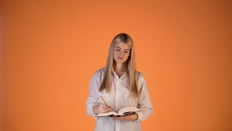 Joven-Rubia-Escribiendo-Notas-En-Un-Cuaderno-De-Papel-Y-Pensando,-Foto-De-Estudio-De-Ilustración-Académica