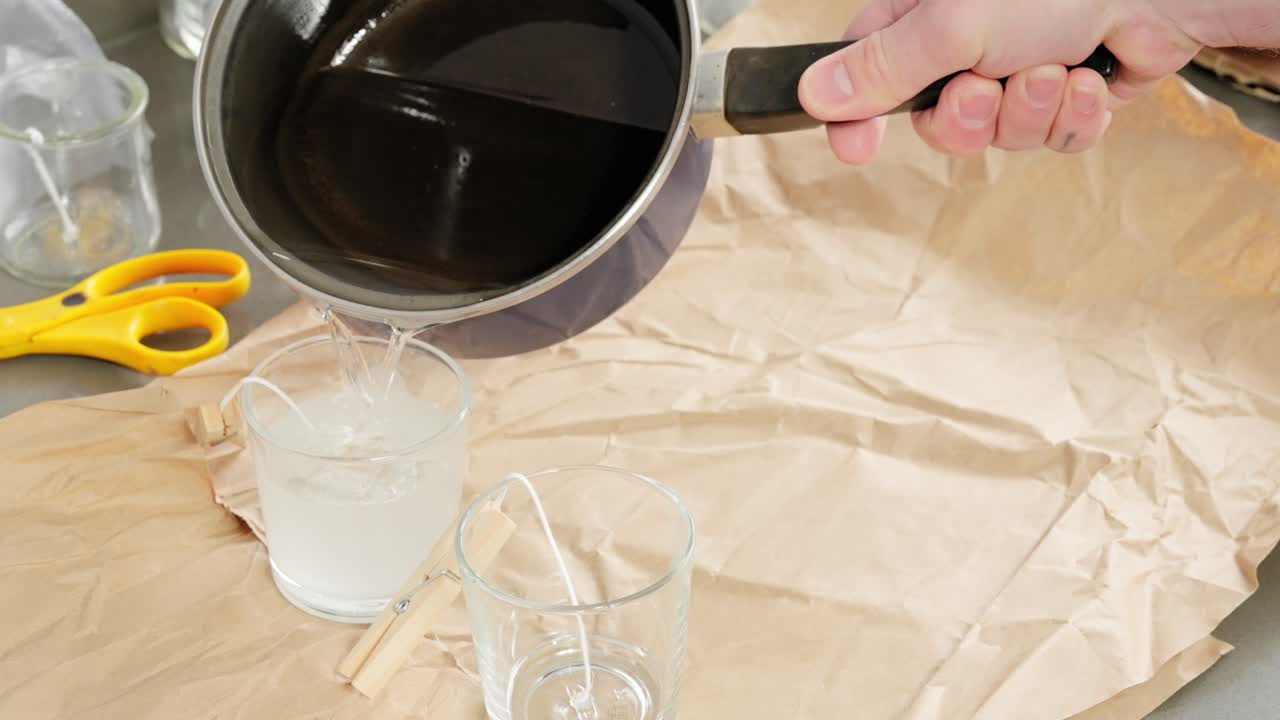 verter cera derretida para hacer velas caseras: sujetar las mechas con pinzas para la ropa