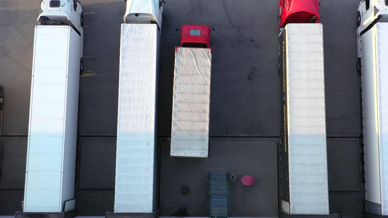 많은 트럭이 상품을 하역하고 있는 산업 창고 보관 건물 적재 구역을 떠나는 세미 트레일러가 부착된 트럭의 항공 샷