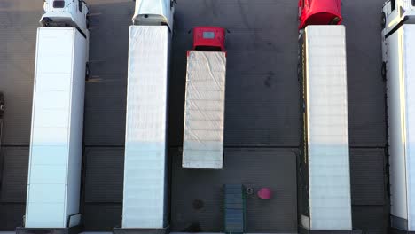 toma aérea de un camión con un semirremolque adjunto que sale del área de carga del edificio de almacenamiento industrial donde muchos camiones están cargando y descargando mercancías