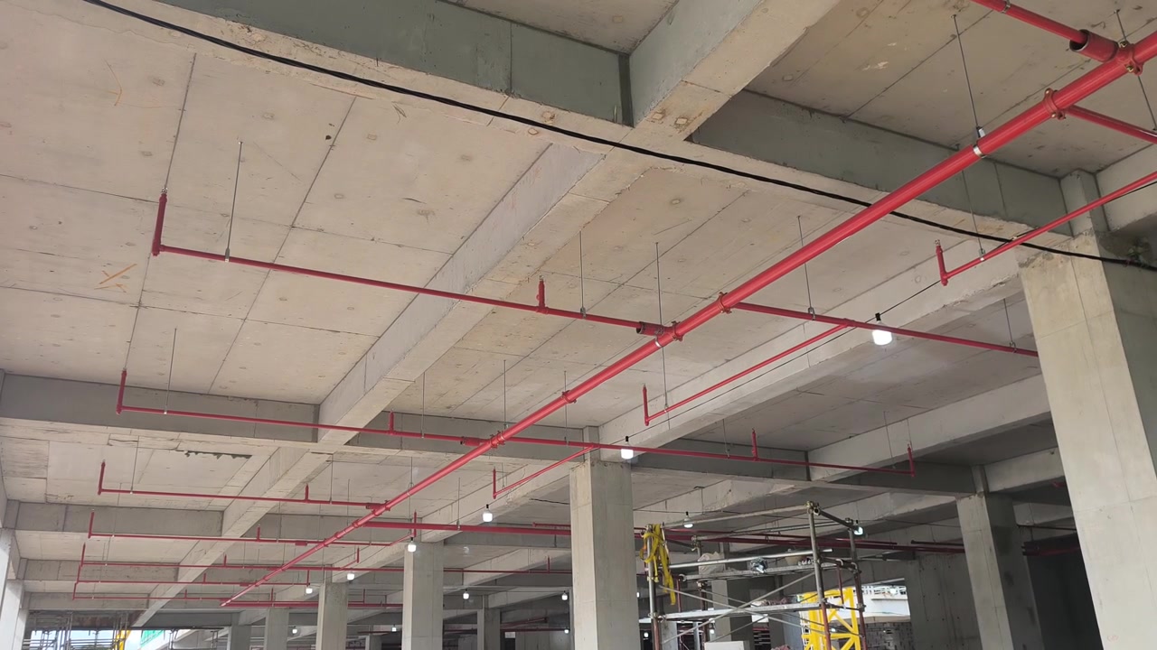 Operai installano una rete di tubazioni antincendio sprinkler in un cantiere edile. Realizzato secondo precisi progetti ingegneristici, questo sistema vitale eroga acqua per sopprimere gli incendi iniziali prima dell'arrivo dei vigili del fuoco