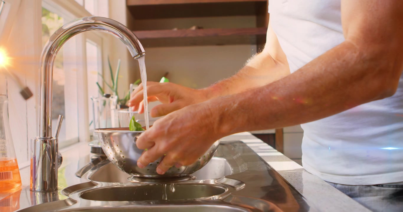 Animazione di punti luce e scie su un uomo caucasico che lava le verdure in cucina