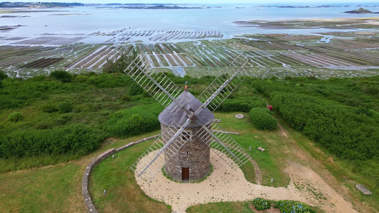 Slow circular drone shot of Craca windmill with oyster beds and sea in the background - France