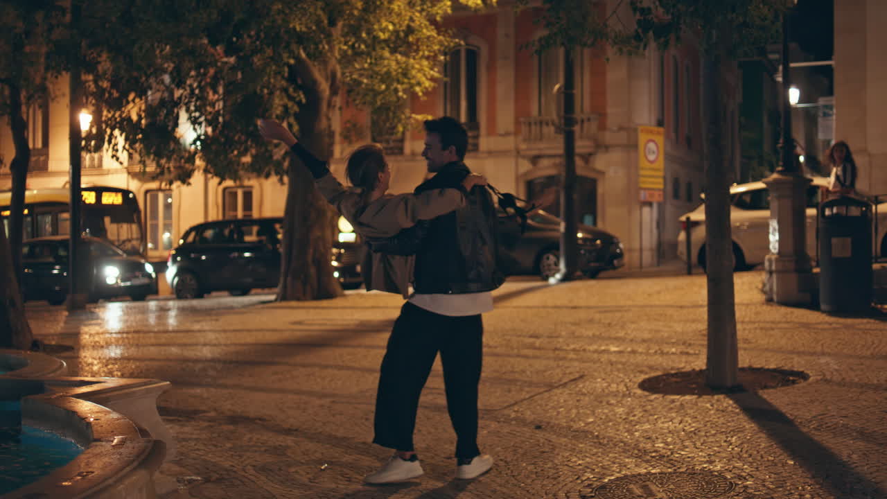 Happy guy spinning girl holding on hands on city street. Carefree lovers on date