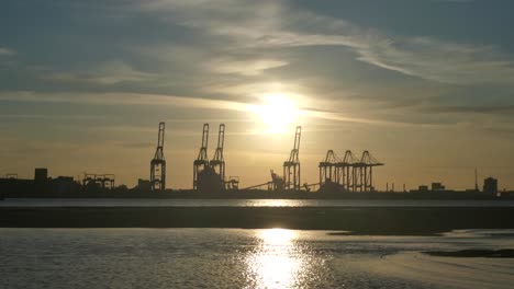 shimmering sunset golden river water with british harbour port cranes silhouettes skyline wide shot