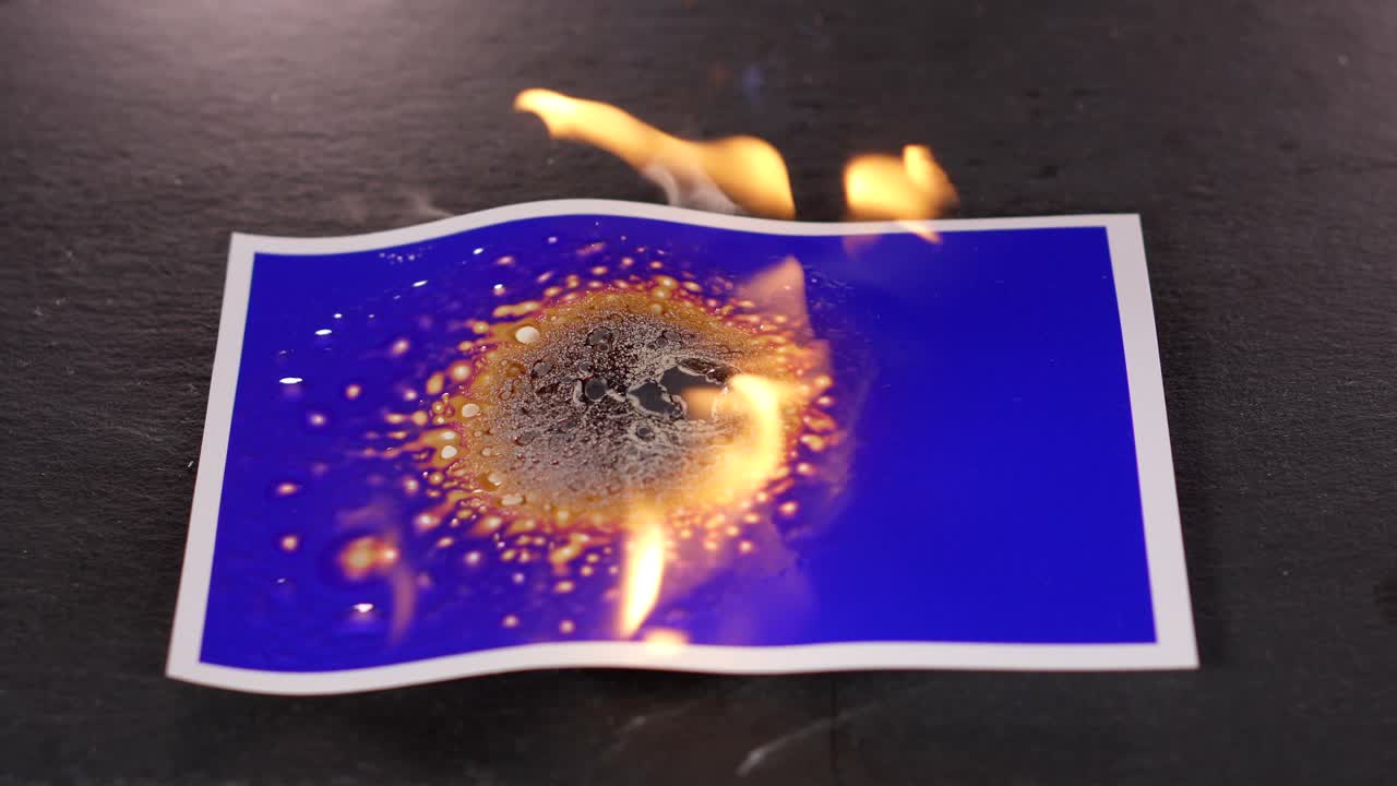 quemar fotografía azul en el fuego en un fondo negro con un quemador de gas. la vieja tarjeta azul está quemada. el fondo de su imagen derrite plástico de la temperatura caliente del gas y el fuego
