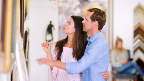una joven pareja blanca discutiendo pinturas en una galería de arte.