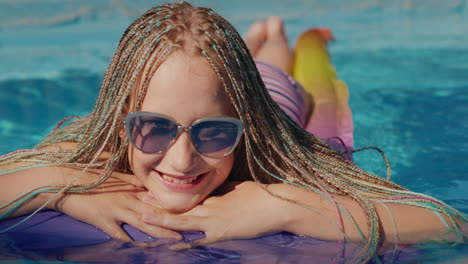 Portrait-of-a-girl-with-afro-pigtails,-swims-on-an-inflatable-mattress-in-the-pool,-resting-and-enjoying-the-rest