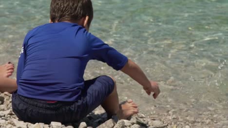 Niño-Caucásico-Jugando-Con-Guijarros-En-La-Playa-De-Fragolimano,-Corinto,-Grecia