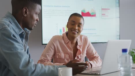 Smiling-african-american-male-and-female-colleague-in-discussion-at-meeting-using-laptop-and-screen