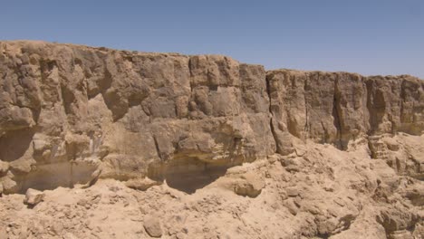 drone tracking along bare eroded brown cliff wall in arid desert region