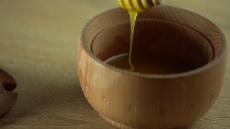 Honey-dripping,-pouring-from-honey-dipper-in-wooden-bowl.-Close-up.-Healthy-organic-Thick-honey-dipping-from-the-wooden-honey-spoon,-closeup.-4K-UHD-video-footage.-Slow-motion