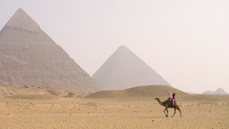Local People With Camel In Front Of The Great Pyramid Of Giza In Egypt. Wide Shot