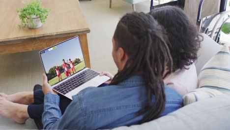 Biracial-couple-laptop-with-diverse-male-soccer-players-playing-match-on-screen