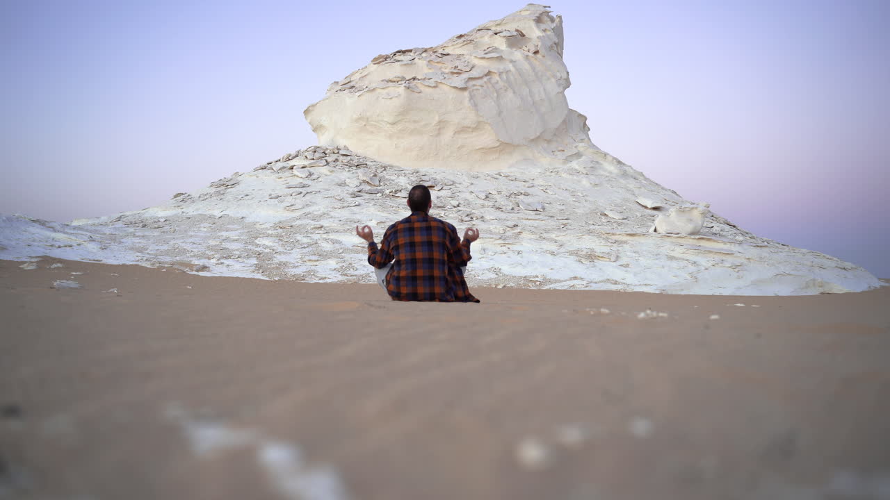 Giovane viaggiatore caucasico nel Parco Nazionale del Deserto Bianco, Egitto, seduto davanti al tramonto, contempla la bellezza di Madre Terra.