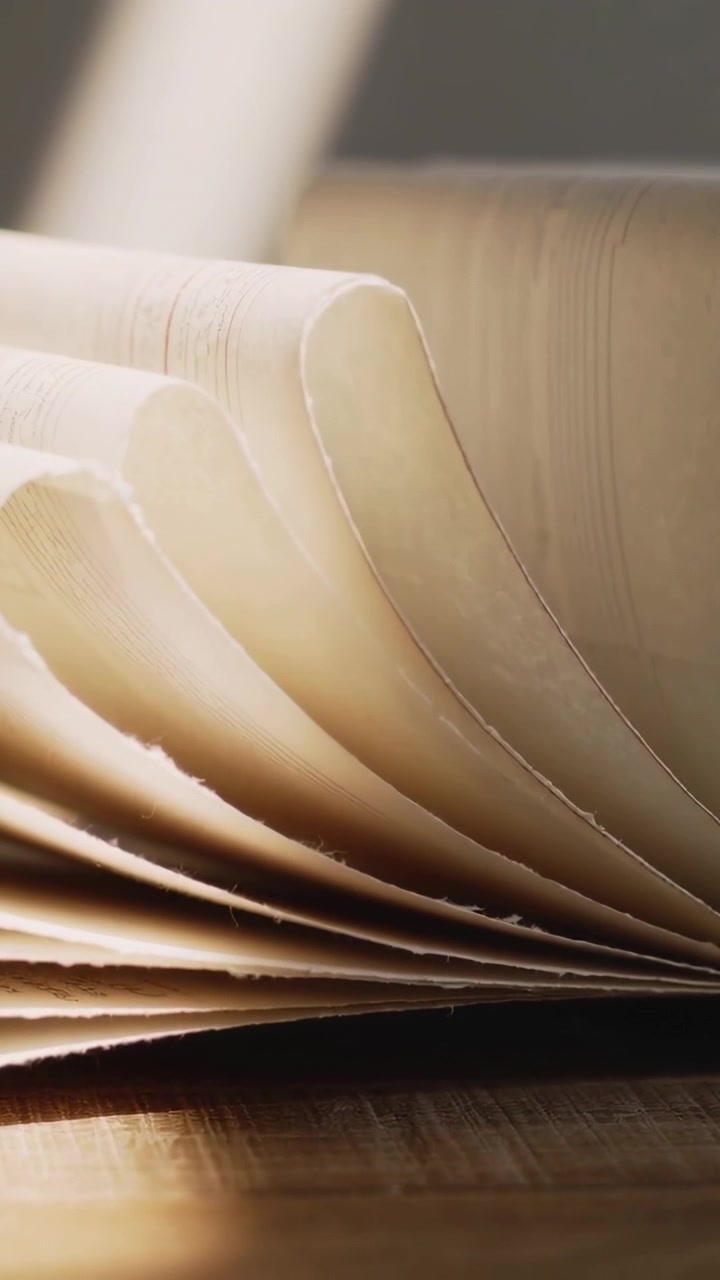 Vertical video: Curling pages settling on wood table by window as sunlight shifting shadows