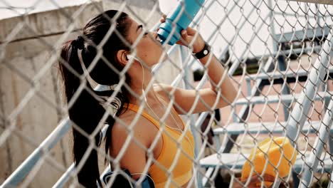 athletic woman drinking water and listening to music after workout